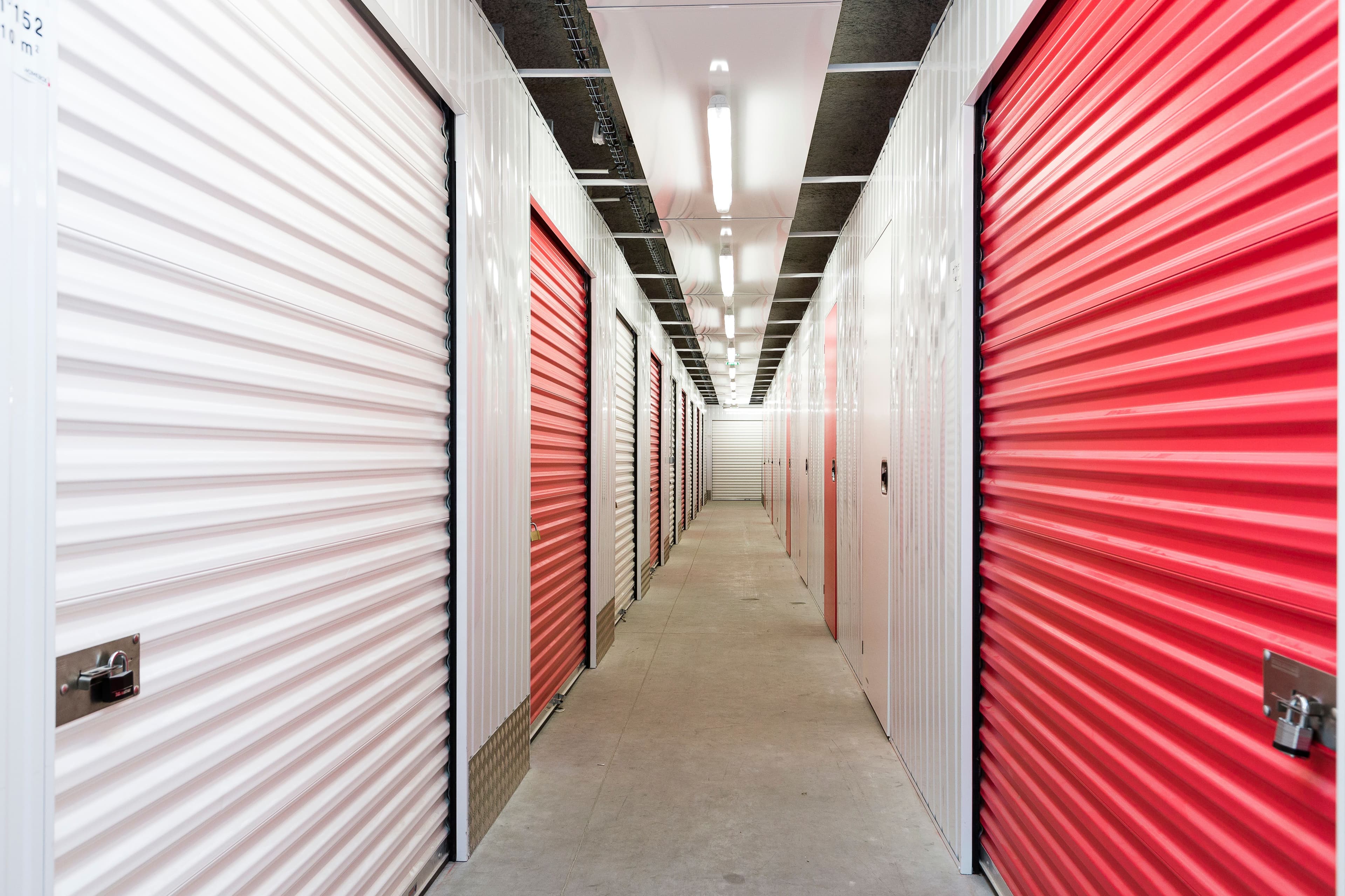 Couloir de box de stockage du centre HOMEBOX Alcalá de Henares avec portes roulantes rouges et blanches.