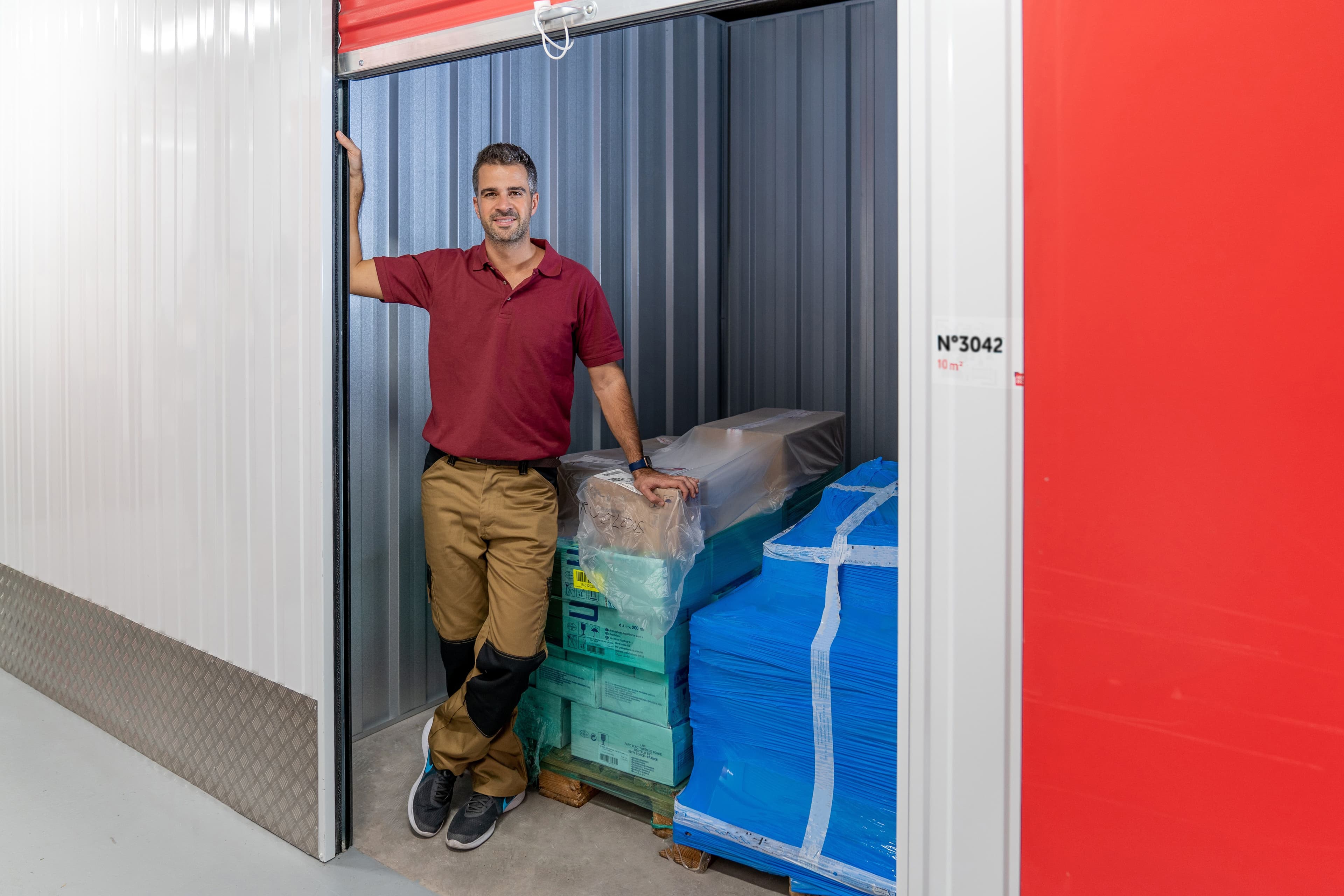 Client professionnel devant son box de stockage HOMEBOX rempli de cartons et matériel protégé, dans un couloir sécurisé.